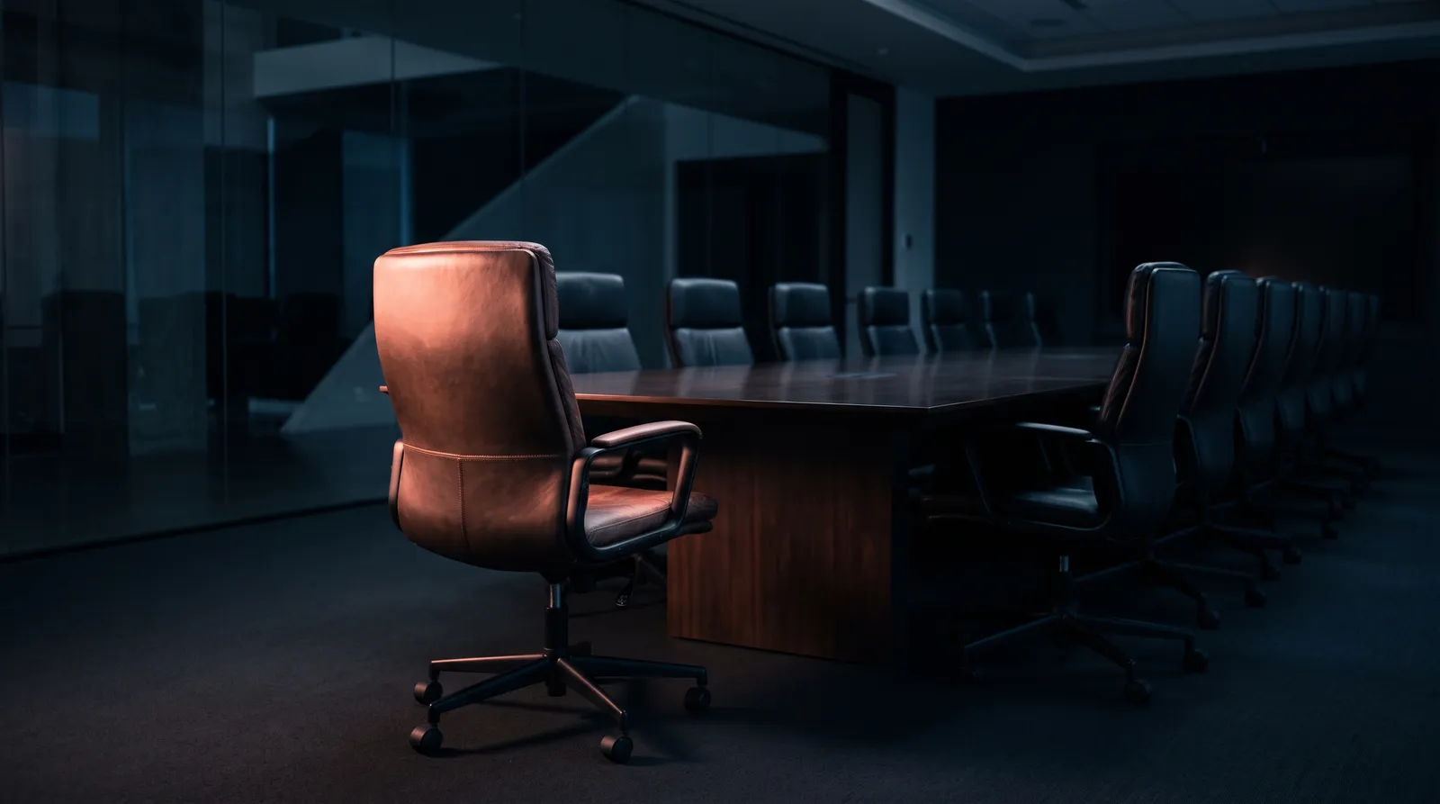 Un fauteuil de bureau vide tourné vers une table de réunion sombre, éclairé de côté par une seule lumière corail