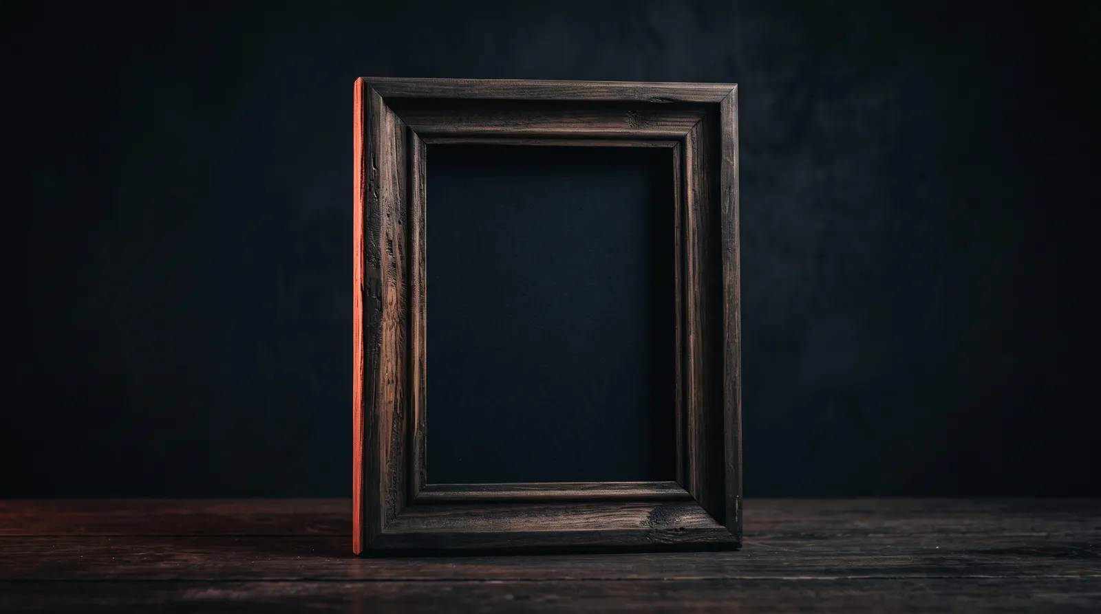 Un cadre de fenêtre en bois posé sur un bureau dans le noir, ne montrant que le mur derrière lui, éclairé par une seule lumière corail rasante