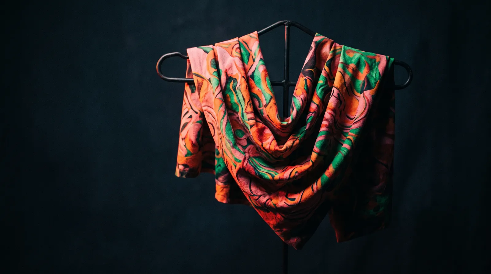 Un tissu à motifs vifs suspendu dans le noir, éclairé par une seule lumière corail rasante