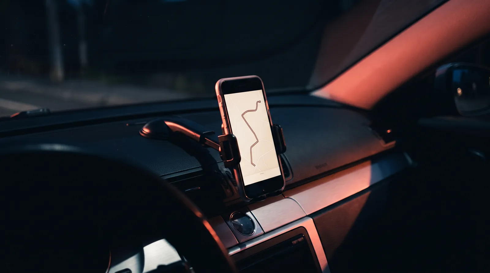 Un téléphone fixé sur un tableau de bord dans la pénombre, affichant un itinéraire, éclairé par une lumière corail rasante