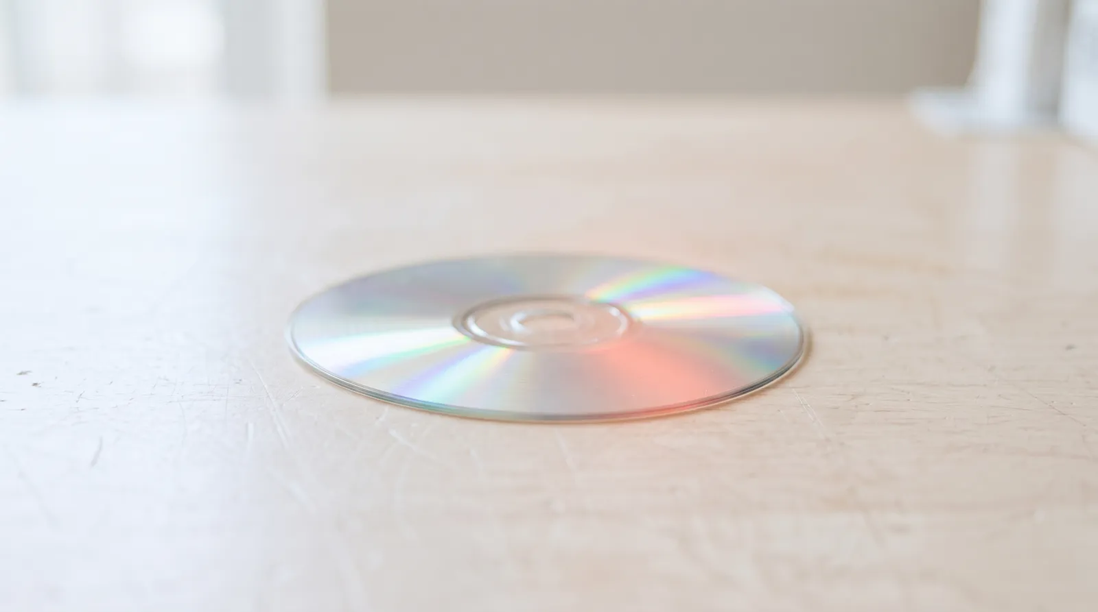 Un CD-ROM posé sur un établi sombre, sa surface irisée accrochant une seule lumière corail rasante
