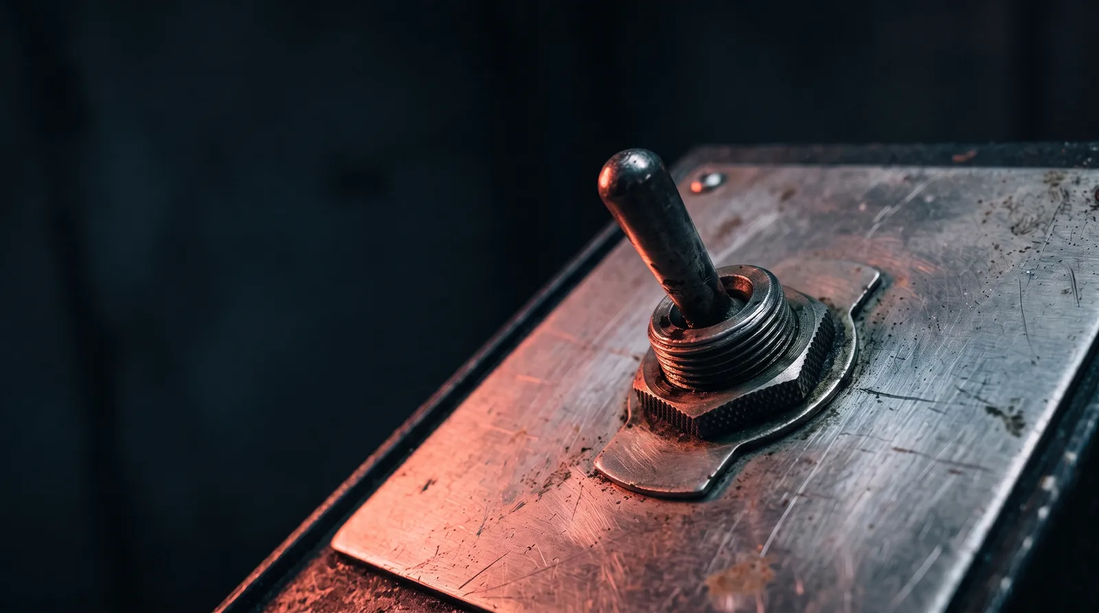 Un interrupteur à bascule industriel en gros plan, dans le noir, éclairé par une seule lumière corail rasante