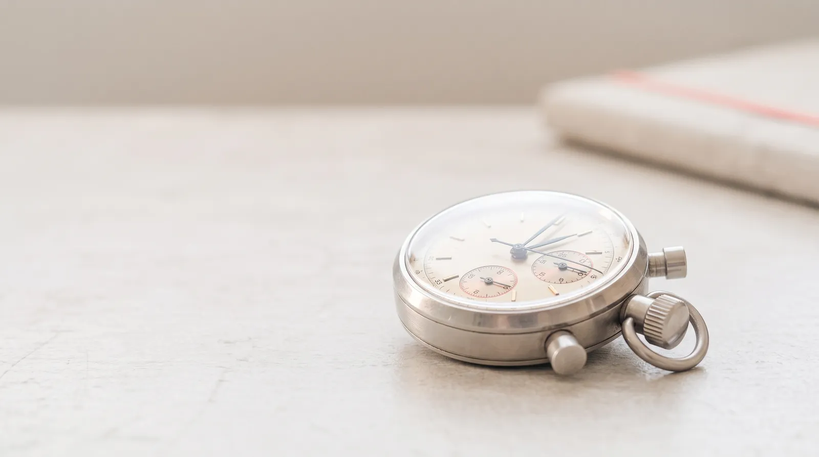 Un chronomètre mécanique de poche posé sur une surface sombre, éclairé par une seule lumière corail rasante