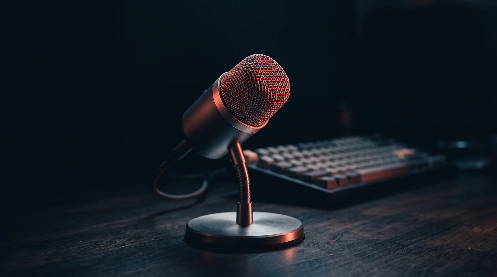 Un microphone de bureau posé devant un clavier mécanique dans l'obscurité, éclairé par une seule lumière corail rasante
