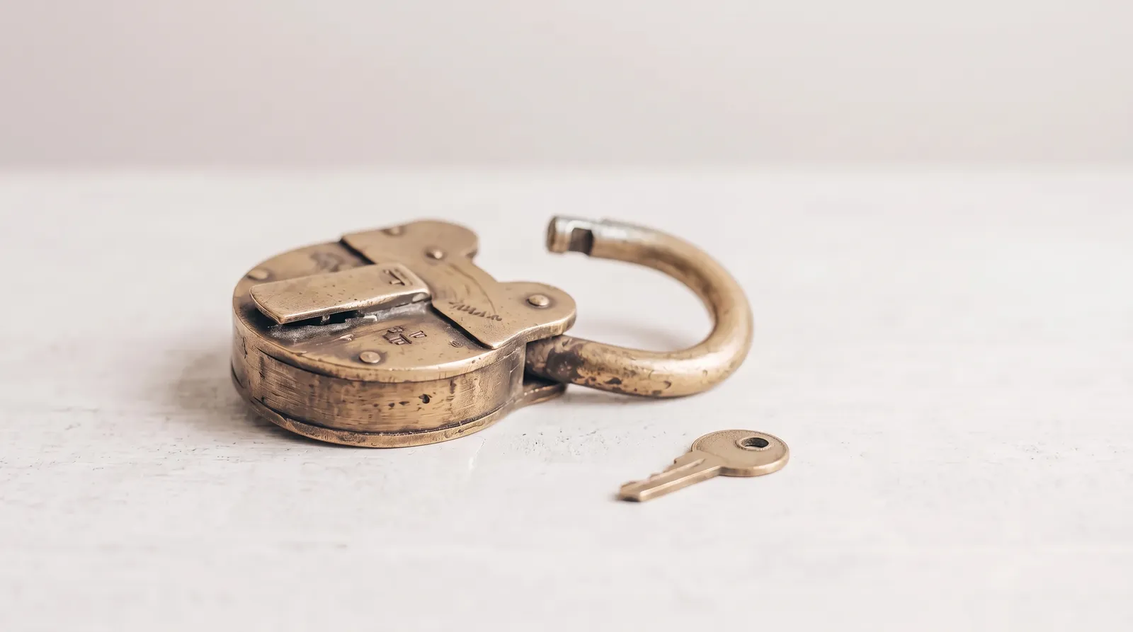 Un vieux cadenas en laiton ouvert, posé sur une table noire, sa clé restée à côté, sous une seule lumière corail