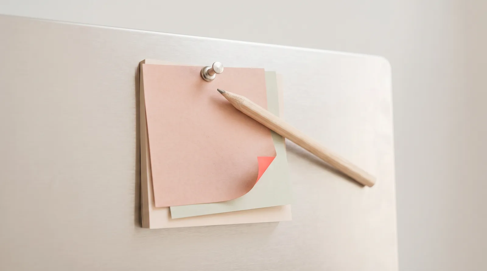 Des papillons adhésifs de couleurs empilés et épinglés sur une plaque métallique, un crayon posé en travers, sous une seule lumière corail rasante dans l'obscurité