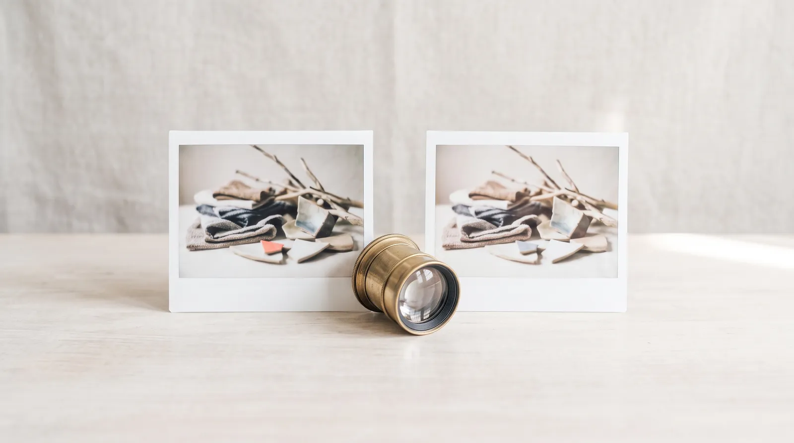 Deux tirages photo posés côte à côte sur un bureau en bois, une loupe de photographe en laiton entre eux, dans le noir, éclairés par une seule lumière corail