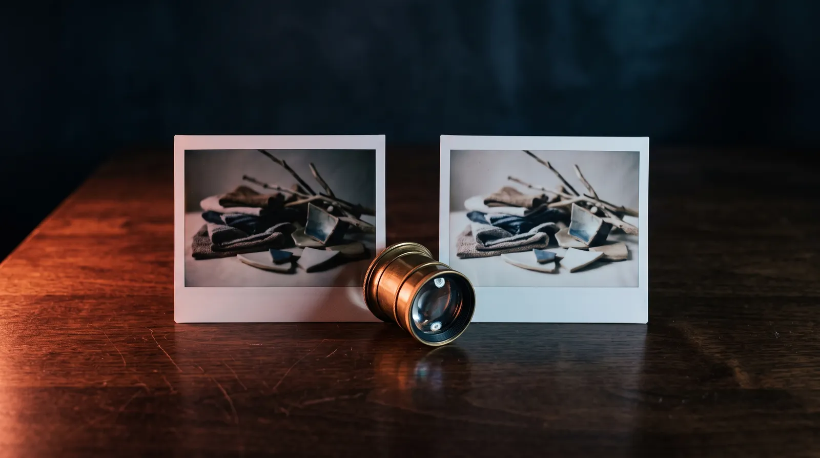 Deux tirages photo posés côte à côte sur un bureau en bois, une loupe de photographe en laiton entre eux, dans le noir, éclairés par une seule lumière corail